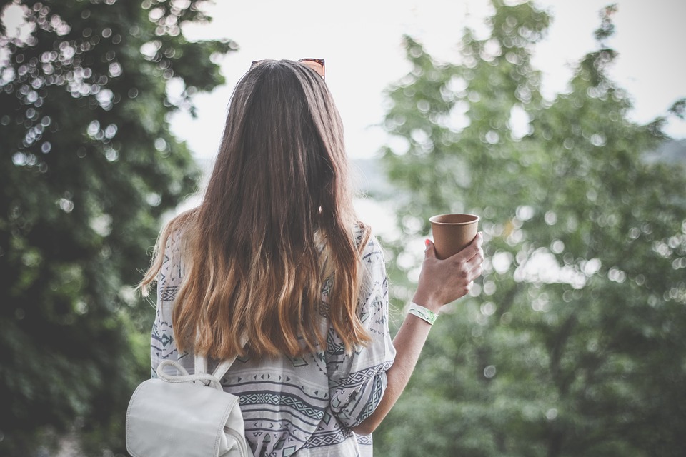 Woman holding cup looking at trees in forest
