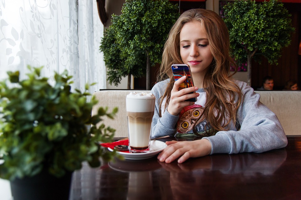 Young woman in cafe with drink on mobile phone